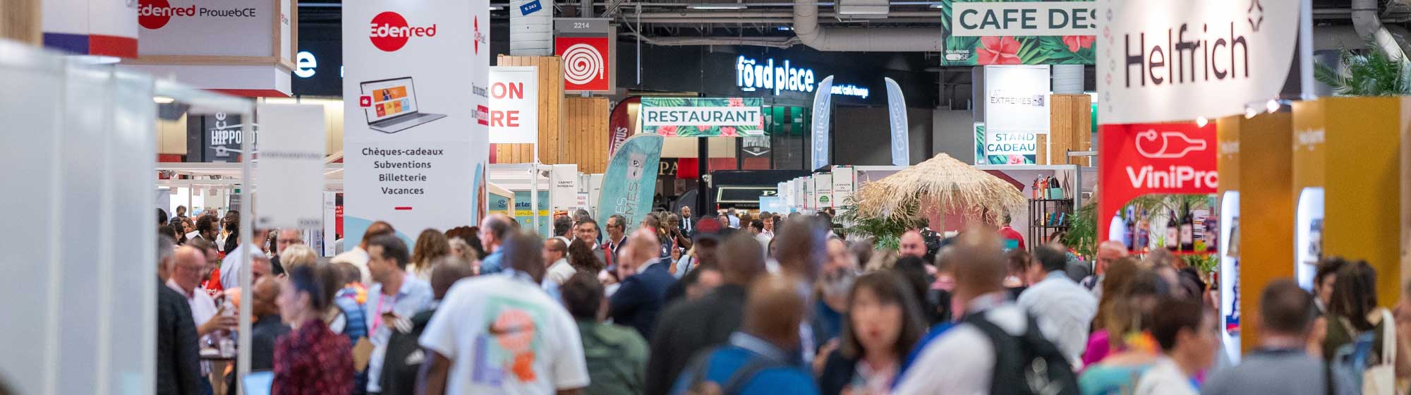 Photographie d'une foule avec plusieurs pancartes au nom des différentes entreprises qui exposent sur le salon